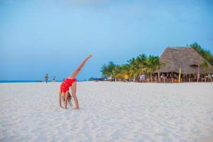 Adorable little girl having fun making cartwheel on tropical beach at sunset photo