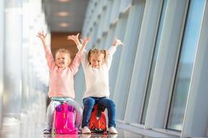 Adorable little girls having fun in airport sitting on suitcase waiting for boarding photo