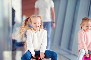 Adorable little girls having fun in airport sitting on suitcase waiting for boarding photo