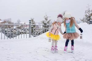 Adorable girls skating on ice rink outdoors in winter snow day photo