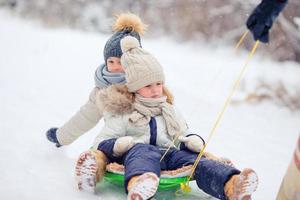 Adorable little happy girls sledding in winter snowy day. photo