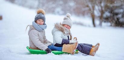 Adorable little happy girls sledding in winter snowy day. photo