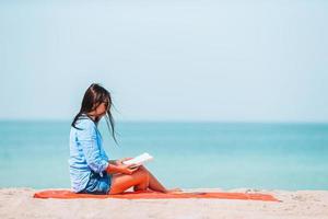 joven leyendo un libro durante la playa blanca tropical foto
