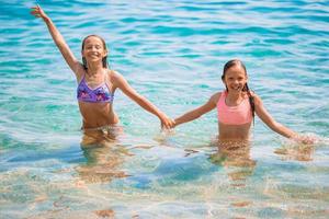 niños felices chapoteando en las olas durante las vacaciones de verano en la playa tropical. las niñas juegan en el mar. foto