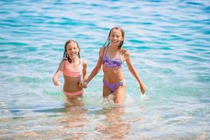 Happy children splashing in the waves during summer vacation on tropical beach. Girls play at the sea. photo