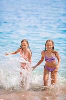 Happy children splashing in the waves during summer vacation on tropical beach. Girls play at the sea. photo