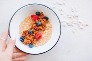 Oatmeal porridge in bowl topped with fresh blueberries, cranberries and homemade crunchy granola photo