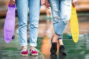 dos chicas hipster con monopatín al aire libre a la luz del atardecer. patinetas de primer plano en manos femeninas. mujeres deportivas activas divirtiéndose juntas en el parque de patinaje. foto