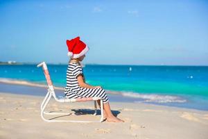Little adorable girl wearing Santa hat at caribbean beach photo