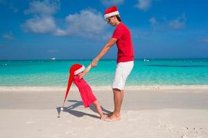 niñita y papá feliz con sombrero de santa se divierten en la playa tropical foto