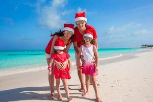 Happy family of four on beach in red Santa hats photo