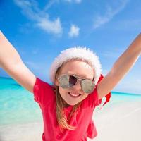 Little adorable girl in red Santa hat have fun on the beach photo