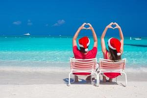 Happy romantic couple in red Santa Hats at beach making hearts photo