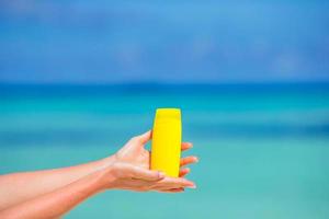 Female hands with suncream bottle background blue sea photo