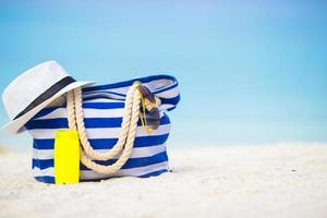 Blue bag, straw hat, sunglasses and sunscreen bottle on white beach photo