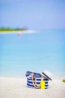 Blue bag, straw hat, sunglasses and sunscreen bottle on white beach photo