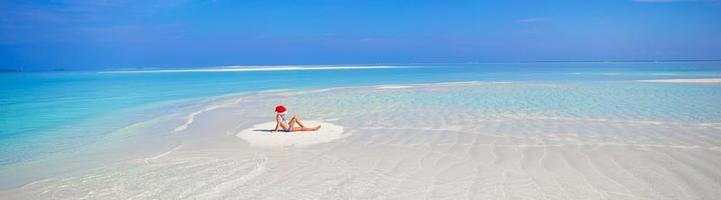 Adorable little girl in Santa hat on the beach during vacation photo