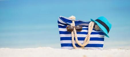 Beach accessories - blue bag, straw hat, sunglasses on white beach photo