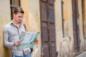 hombre turista con un mapa de la ciudad y una mochila en la calle europa. niño caucásico mirando con mapa de ciudad europea en busca de atracciones. foto