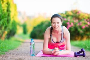 Sport fitness girl training push-ups. Female athlete exercising push up outside in empty park. Fit model in crossfit exercise outdoors. Healthy lifestyle concept. photo