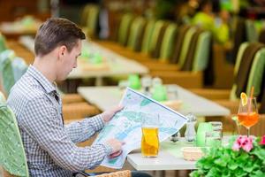 Caucasian young european man with citymap in outdoors cafe. Portrait of attractive young tourist on lunch time photo