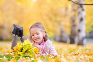 retrato de niña adorable con ramo de hojas amarillas en otoño. hermoso niño sonriente acostado en la alfombra de hojas