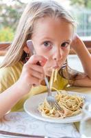 Adorable little girl eating spaghetti in outdoors restaraunt photo