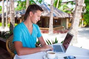 Young businessman using laptop during summer tropical vacation photo