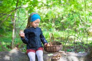Little girl gathering mushrooms in autumn forest photo