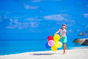 Little girl playing with colorful balloons at tropical beach photo
