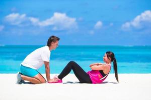 Young fitness couple doing side crunches on white beach during vacation photo