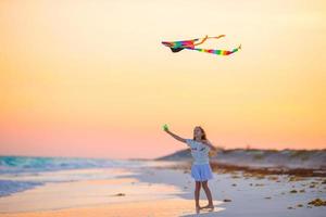 niña con cometa voladora en playa tropical al atardecer. juego de niños en la orilla del océano. niño con juguetes de playa. foto