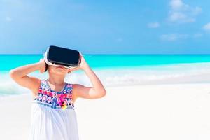 Little girl using VR virtual reality goggles. Adorable kid look into the virtual glasses on white beach photo