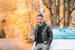 joven bebiendo café con teléfono en el parque de otoño al aire libre foto