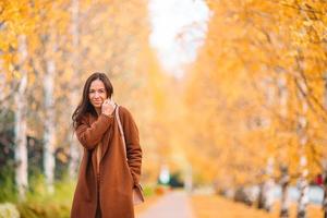 Fall concept - beautiful woman drinking coffee in autumn park under fall foliage photo