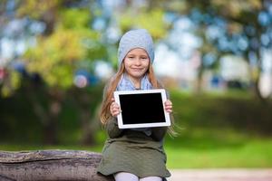 Adorable little girl holding tablet PC outdoors in autumn sunny day photo