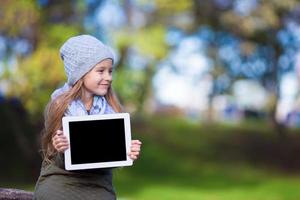 adorable niña sosteniendo tablet pc al aire libre en un día soleado de otoño foto