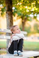 Adorable little girl at beautiful autumn day outdoors. Little girl on the bench in fall photo