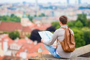Young man with a city map and backpack background european city. Caucasian tourist looking at the map of European city with beautiful view of attractions. photo