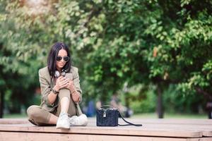 Cute woman is reading text message on mobile phone while sitting in the park. photo