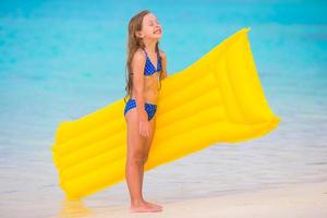 Adorable happy girl with inflatable air mattress on white beach photo