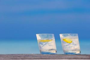 Glasses of waters with lemon on wooden on sea background photo