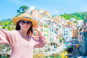 Young woman taking selfie with beautiful view at old italian village Riomaggiore, Cinque Terre, Liguria, Italy. European italian vacation. photo