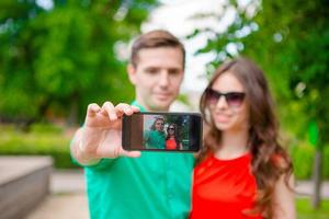 Couple taking a selfie by smartphone. Young man making photowith girlfriend on the street laughing and having fun in summer. photo