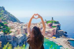 hermosa chica haciendo con las manos en forma de corazón en el fondo de la antigua ciudad costera de vernazza, parque nacional de cinque terre, liguria, italia, europa foto