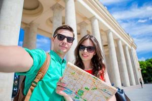 Young tourist friends traveling on holidays in Europe smiling happy. Caucasian family with city map making selfie background of attractions photo