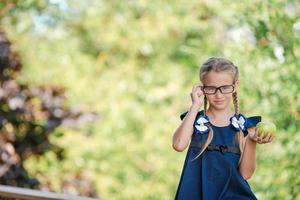 Adorable little school girl with green apple outdoor. Back to school concept photo