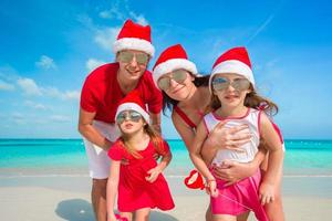 retrato de familia feliz en la playa con sombreros de navidad foto