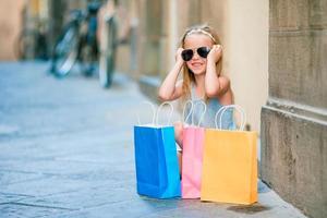 Portrait of adorable little girl walking with shopping bags outdoors in european city. photo