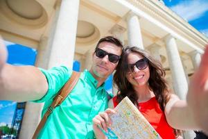 jóvenes amigos turistas que viajan de vacaciones en europa sonriendo felices. familia caucásica con mapa de la ciudad haciendo selfie fondo de atracciones foto